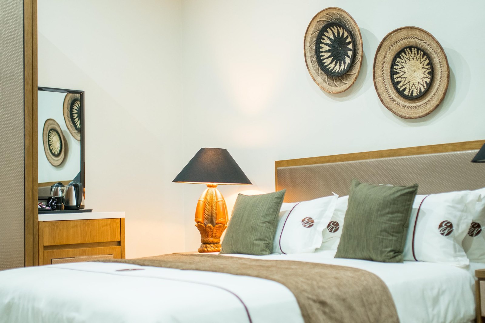 Ezulwini Villa bedding with sage cushions, a carved lamp and woven wall details